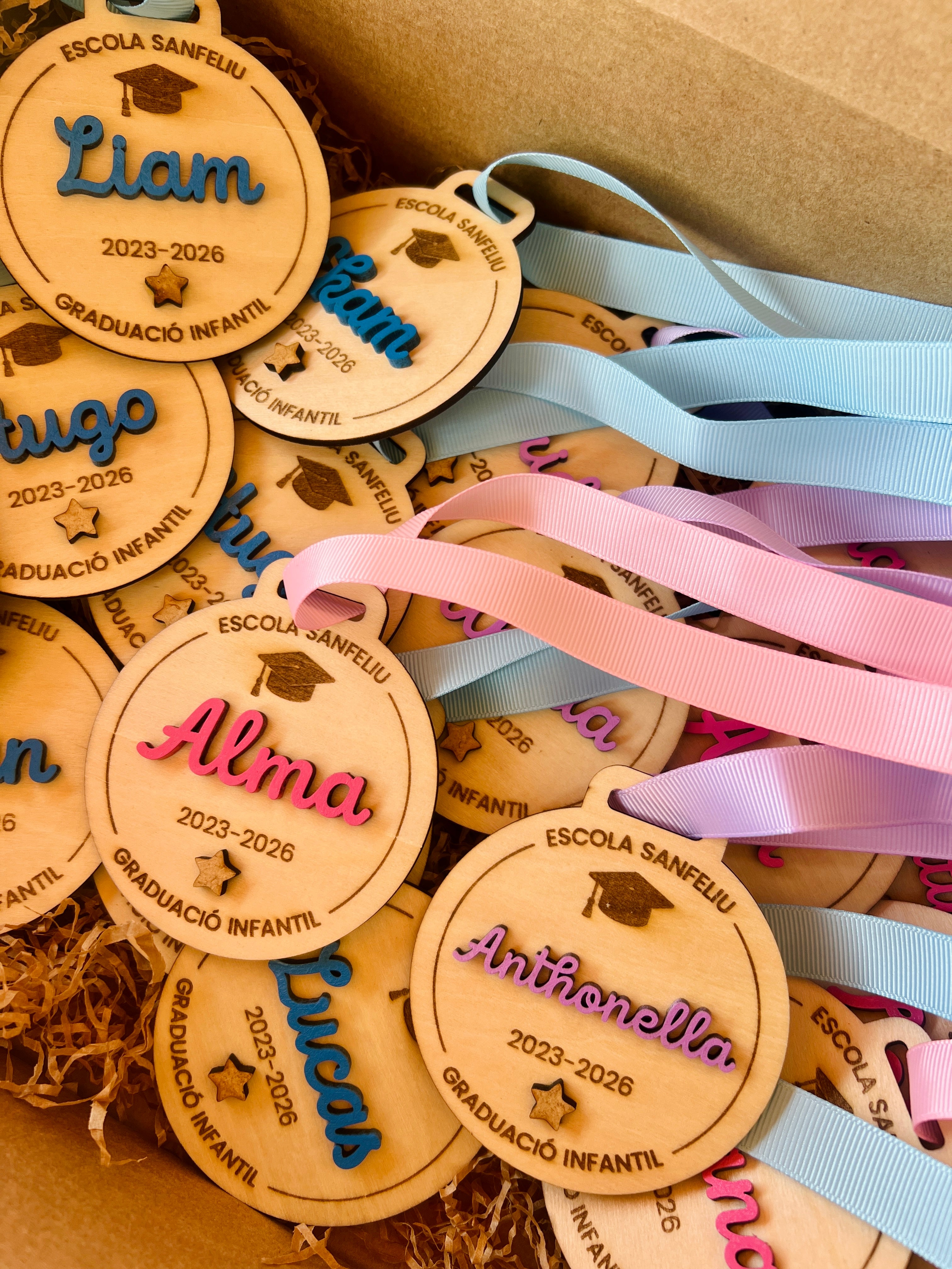 Medallas personalizadas madera fin de curso con nombres Liam, Alma y Anthonella, cintas rosa y azul